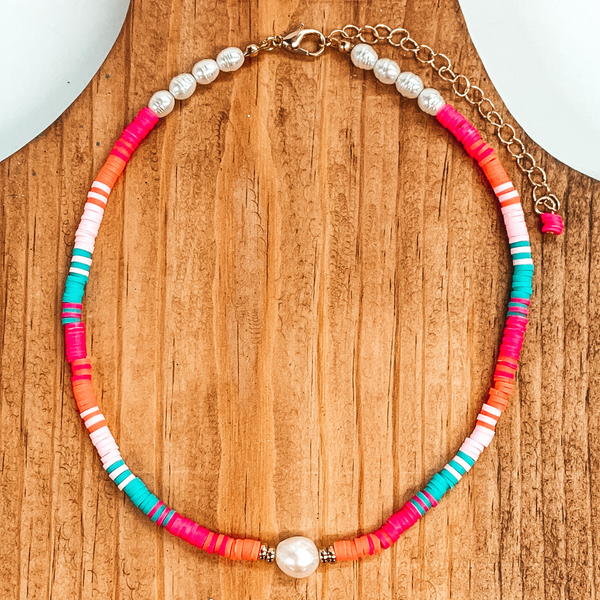Thin rubber beads with a center white pearl and four pearls on either sides of the clasp. This necklace includes the colors light blue, hot pink, light pink, and orange. This necklace is pictured on a brown block on a white background. 