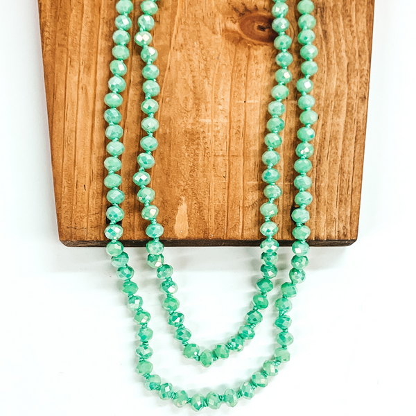Crystal beaded necklace in seafoam green. This necklace is pictured laying on a brown block on a white background.