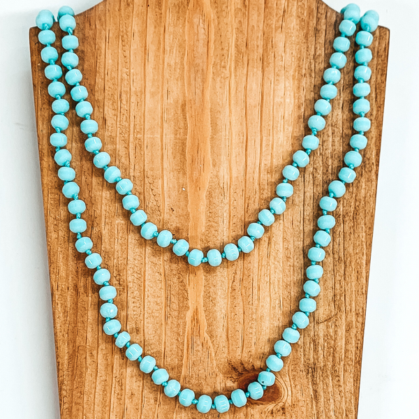 Crystal beaded necklace in druzy sky blue. This necklace is pictured laying on a brown necklace holder on a white background.