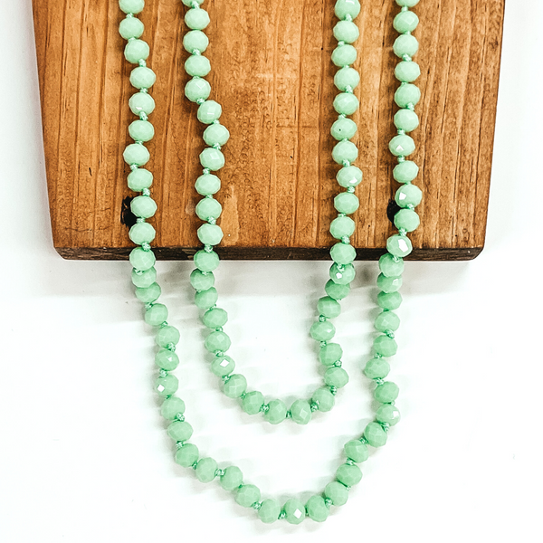 Crystal beaded necklace in mint. This necklace is pictured laying on a brown block on a white background.