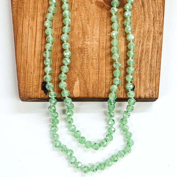 Crystal beaded necklace in jadeite green. This necklace is pictured laying on a brown block on a white background.
