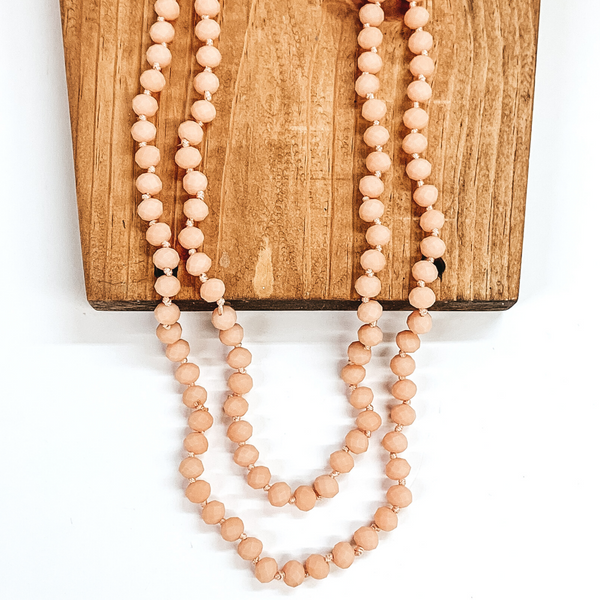 Crystal beaded necklace in matte blush. This necklace is pictured laying on a brown block on a white background.