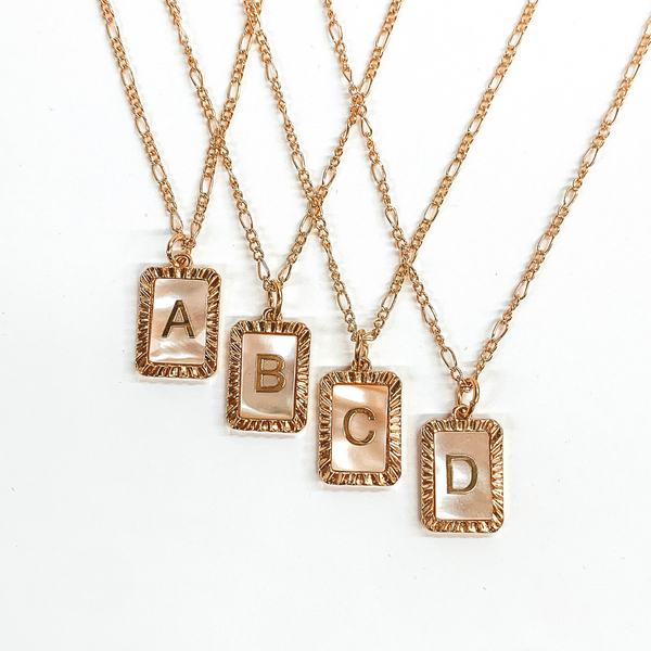 Four gold, figaro chained necklaces with rectangle pendants. Each pendant is outlined with gold and has a ivory shell center with a gold initial. This picture includes the initials "A, B, C, and D." These necklaces are pictured on a white background. 