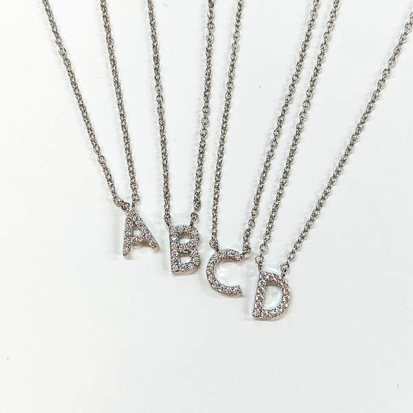 Silver chain initial necklace. Each initial has a clear crystal inlay. The letters included in this picture are "A, B, C, and D." These necklaces are pictured on a white background. 