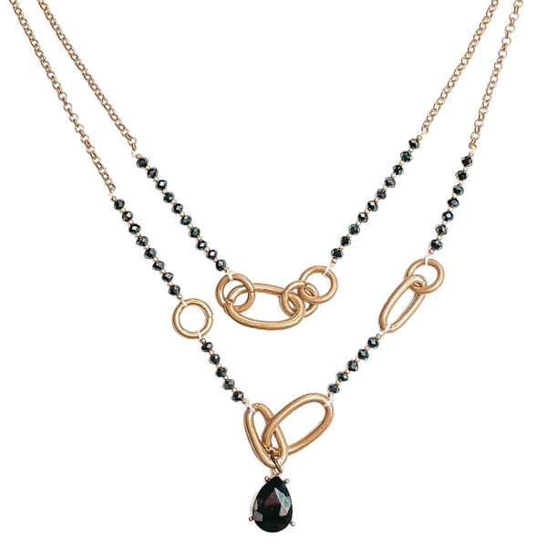 Two stranded necklace that includes a sall gold chiain part, black crystal beaded part, and large gold chain links. This necklace also has a black teardrop crystal pendant. This necklace is pictured on a white background. 