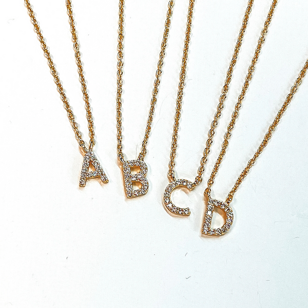 Gold chain initial necklace. Each initial has a clear crystal inlay. The letters included in this picture are "A, B, C, and D." These necklaces are pictured on a white background.