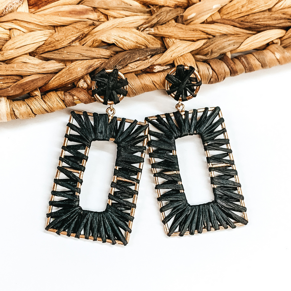 Gold wire circle studs with a gold wire open rectangle drop earrings wrapped in black raffia. These earrings are pictured on on a white background with basket weave decor.