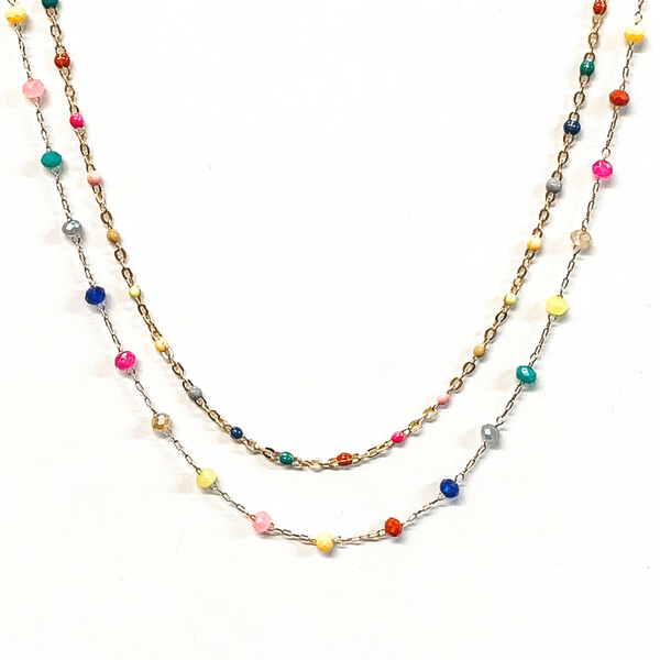 The first strand is a gold chain with small, multicolor bead spacers. The second gold chain has small, crystal bead spacers in a multicolor. This necklace is pictured on a white background.
