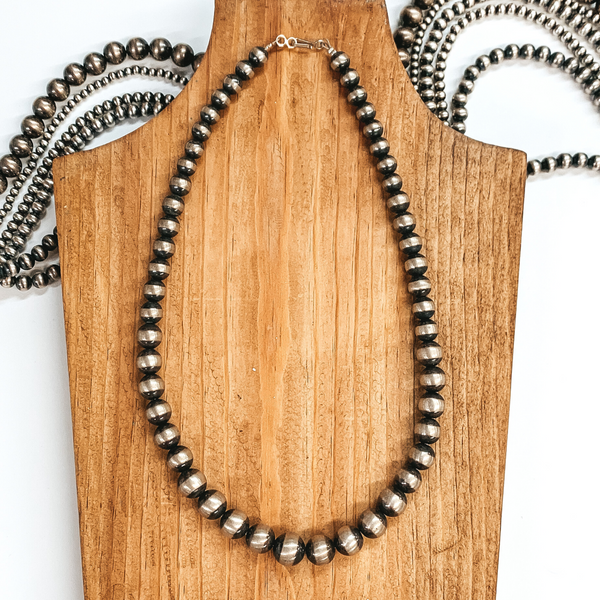 Silver beaded necklace that has beads going from small to bigger beads. This necklace is pictured on a brown necklace holder on a white background that includes silver beads. 