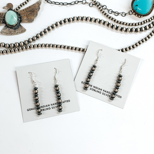 Silver, graduated beads and saucer beaded drop earrings. These earrings are pictured on a white background on top of silver beads. 