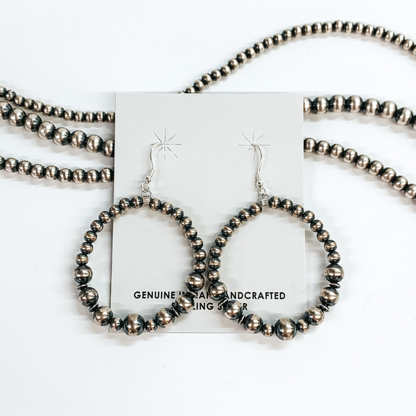 Silver beaded circle drop earrings with silver, tiny, saucer bead spacers. These earrings are pictured on a white background on top of silver beads.