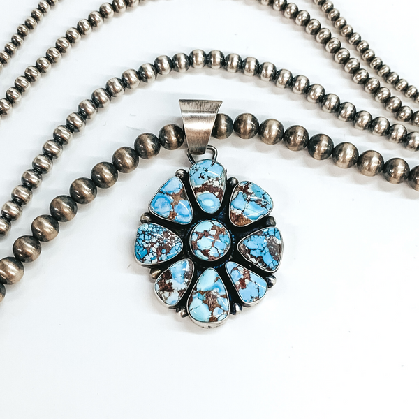 Silver bail with an attached blue turquoise stone cluster. This pendant is pictured on a white background with silver beads above the pendant. 