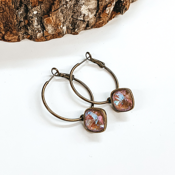 Two bronze hoop earrings with a square cappuccino delight crystal. These earrings are pictured on a white background with a piece of wood at the top.