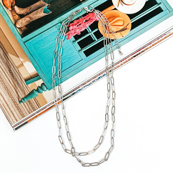 Silver layered paperclip chain necklace that is pictured half on a magazine and half on a white background.