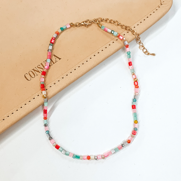 Multicolored beaded necklace that is pictured on a white and tan background. 