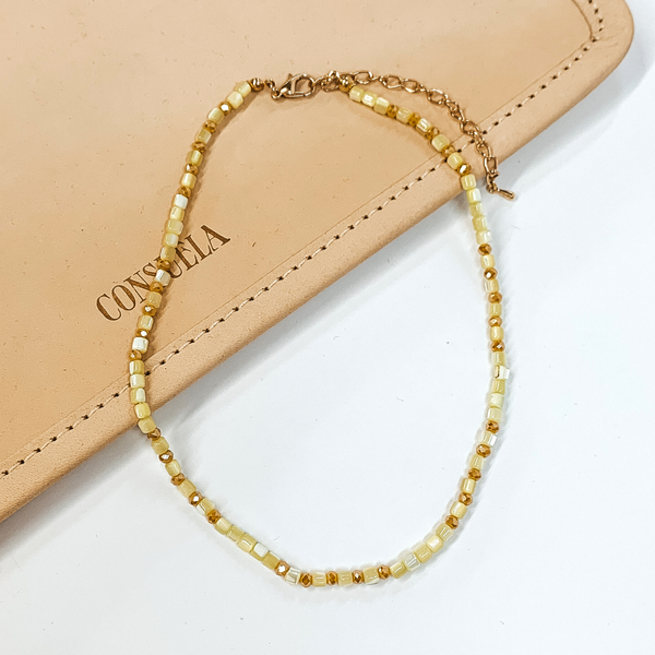 Yellow beaded necklace that is pictured on a white and tan background.