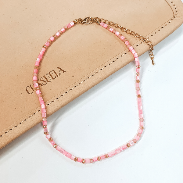 Pink beaded necklace that is pictured on a white and tan background.