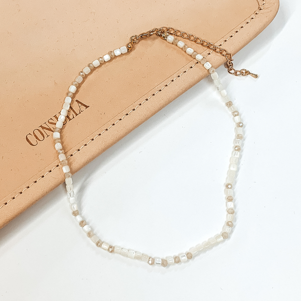 Ivory beaded necklace that is pictured on a white and tan background.