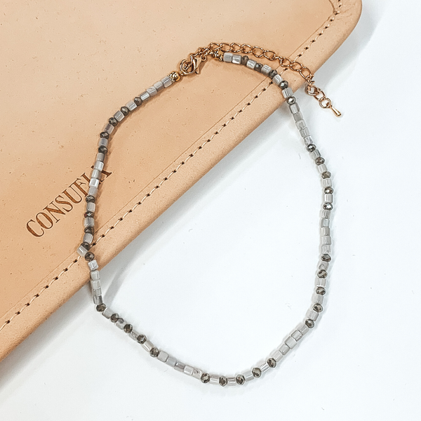 Grey beaded necklace that is pictured on a white and tan background.