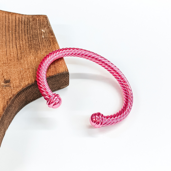 Cable bracelet with cabochon ends in metallic pink. This bracelet is pictured on a white background and leaning on a piece of brown wood. 