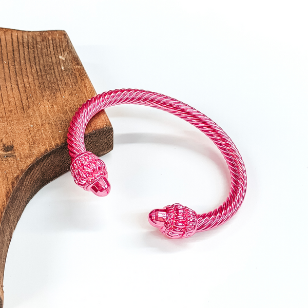 Cable bracelet with big cabochon ends in metallic pink. This bracelet is pictured on a white background and leaning on a piece of brown wood. 