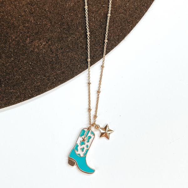 Gold chain necklace with a gold star charm and a white and turquoise cow print boot charm. This necklace is pictured on a white and brown background.