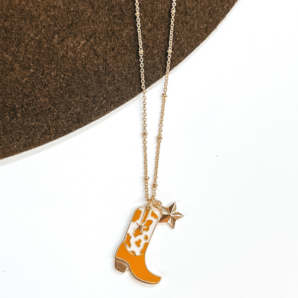 Gold chain necklace with a gold star charm and a white and tan cow print boot charm. This necklace is pictured on a white and brown background.
