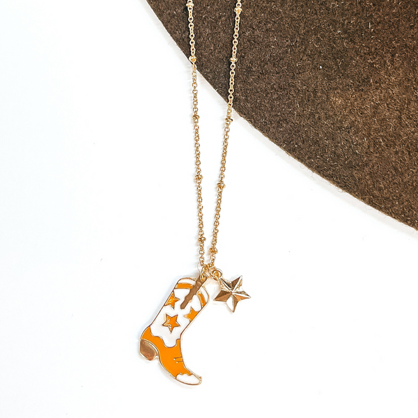 Gold chain necklace with a gold star charm and a ivory and tan star print boot charm. This necklace is pictured on a white and brown background.