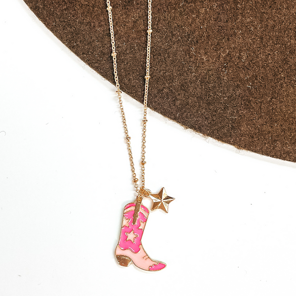 Gold chain necklace with a gold star charm and a white and pink star print boot charm. This necklace is pictured on a white and brown background.