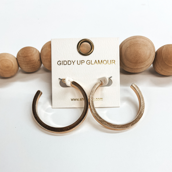 These are large shiny gold hoops with a post back  backing. Taken on a white background and leaned up  against brown wood balls.