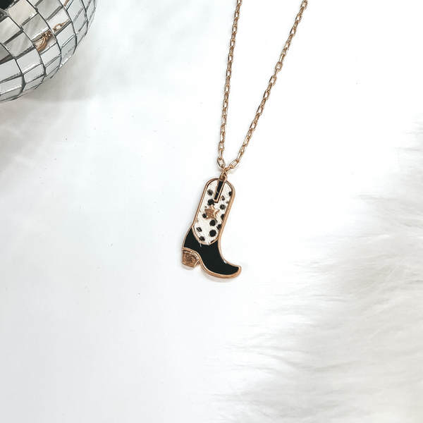 This is a gold chain necklace with a boot pendant in a gold setting. The boot pendant is black and has a dotted print with a gold star. This necklace is taken on laying on a white background with a white fur carpet in the side and two disco ball as decor.