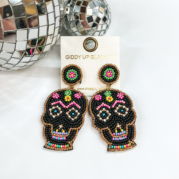 These are seedbeaded sugar skull post earrings in  black with multicolored beads as well. These earrings  are taken on a white background and two disco balls  in the back as decor.