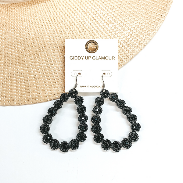Black, open teardrop outline earrings. These  earrings  have tiny, engraved flowers that make out the shape  of a teardrop. The middle of each flower has a black  crystal. These earrings are pictured laying on a  straw hat brim and a white background.