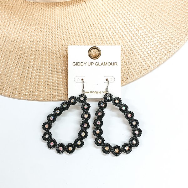 Black, open teardrop outline earrings. These  earrings  have tiny, engraved flowers that make out the shape  of a teardrop. The middle of each flower has an AB  crystal. These earrings are pictured laying on a  straw hat brim and a white background.