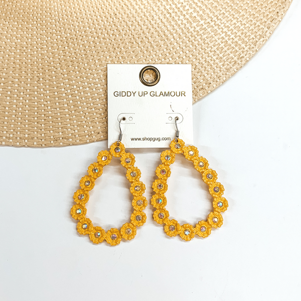 Mustard yellow, open teardrop outline earrings. These  earrings  have tiny, engraved flowers that make out the shape  of a teardrop. The middle of each flower has an AB  crystal. These earrings are pictured laying on a  straw hat brim and a white background.
