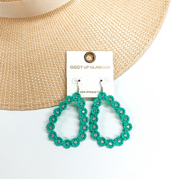 Turquoise, open teardrop outline earrings. These  earrings  have tiny, engraved flowers that make out the shape  of a teardrop. The middle of each flower has an AB  crystal. These earrings are pictured laying on a  straw hat brim and a white background.