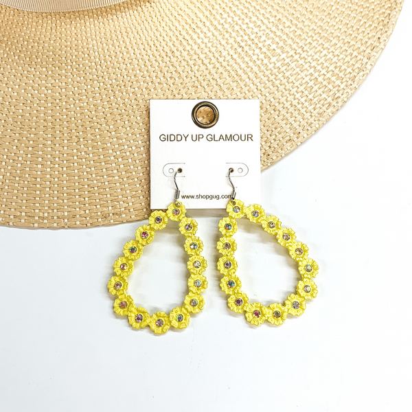 Neon yellow, open teardrop outline earrings. These  earrings  have tiny, engraved flowers that make out the shape  of a teardrop. The middle of each flower has an AB  crystal. These earrings are pictured laying on a  straw hat brim and a white background.