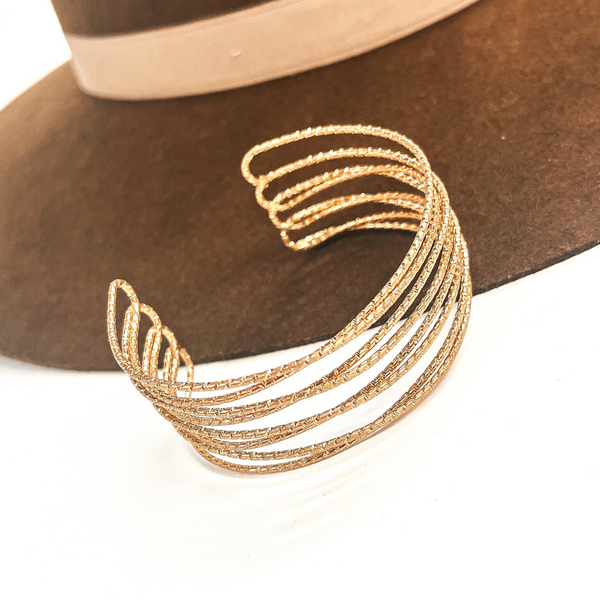 This is a gold cuff bracelet, there are eight layered textured wires.  This cuff bracelet is open ended. This bracelet is taken on a dark brown brim hat and on a white background.