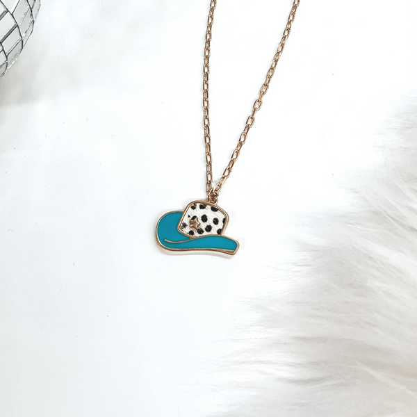 This is a gold chain necklace with a hat pendant in a gold setting. The hat pendant is turquoise and has a dotted print with a gold star. This necklace is taken on laying on a white background with a white fur carpet in the side and two disco ball as decor.