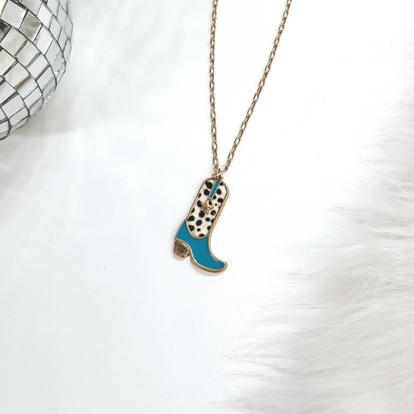 This is a gold chain necklace with a boot pendant in a gold setting. The boot pendant is turquoise and has a dotted print with a gold star. This necklace is taken on laying on a white background with a white fur carpet in the side and two disco ball as decor.