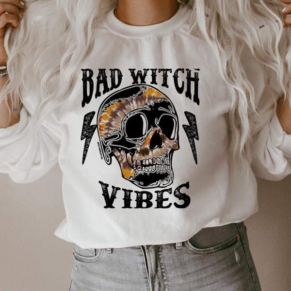 model is wearing a white sweatshirt which reads "bad witch vibes" in black font with a multicolored skull and lightning bolts.