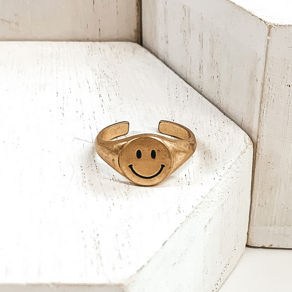 Gold, non adjustable ring with a round smiley face. This ring is pictured on a white block with more white blocks in the background.