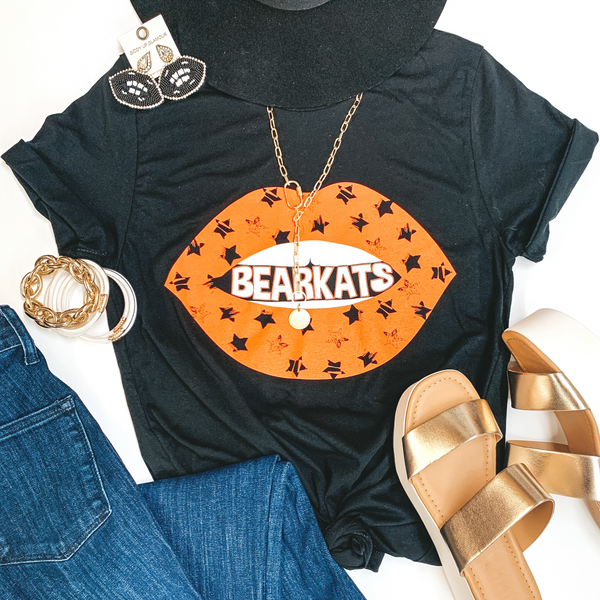 A black tee shirt with short sleeves and an orange lip graphic with black stars that says "Bearkats" in between. Pictured on a white background jeans, gold wedges, gold jewelry, and black earrings.