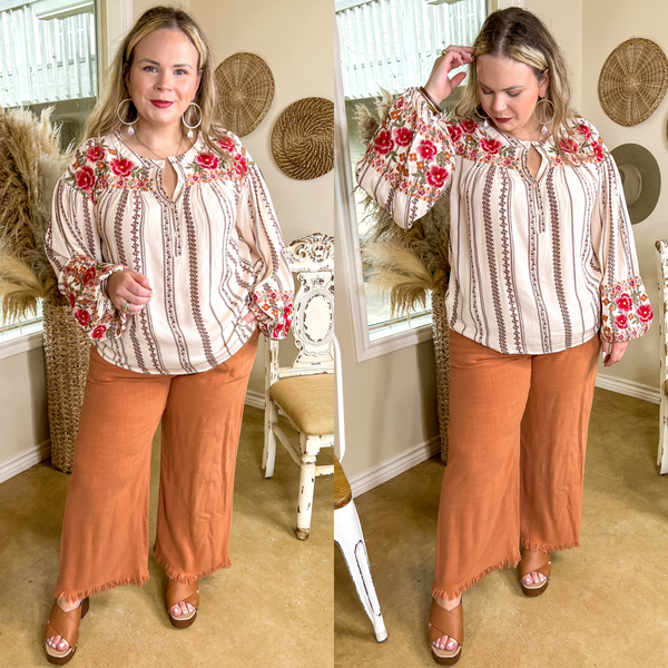 Model is wearing a pair of clay orange linen pants with a frayed hem. Model has it paired with an ivory top, tan wedges, and gold jewelry.