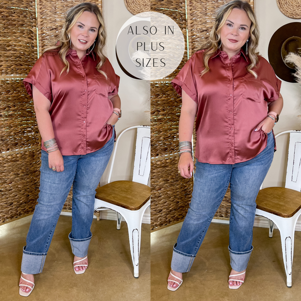 Model is wearing a mauve pink button up top with short sleeves. Model has it paired with cuffed jeans, white heels, and silver jewelry.