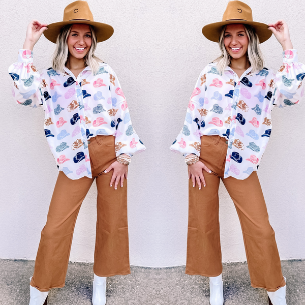 Model is wearing wide leg cropped denim jeans in light brown. Model has it paired with a white, cowboy hat printed top, white booties, and a tan hat. 