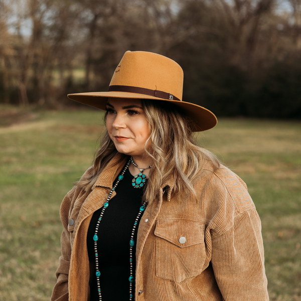 Light Brown Felt Hat with Dark Brown Hat Band with Charlie 1 Horse Pin. Model has it paired with a brown jacket and turquoise jewelry. Pictured on wooded background