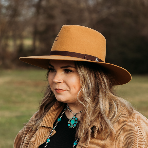 Mustard Yellow Felt Hat with Dark Brown Band and Charlie 1 Horse Pin. Model has it paired with a brown jacket and turquoise jewelry. Pictured on wooded background.