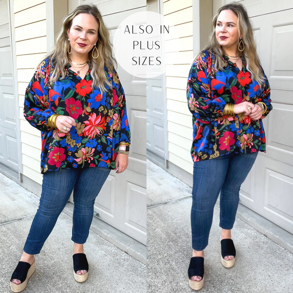 Model is wearing a black top with 3/4 sleeves, a notched neckline, and a bright floral print in red and blue. Model has it paired with dark wash skinny jeans, black wedges, and gold jewelry.