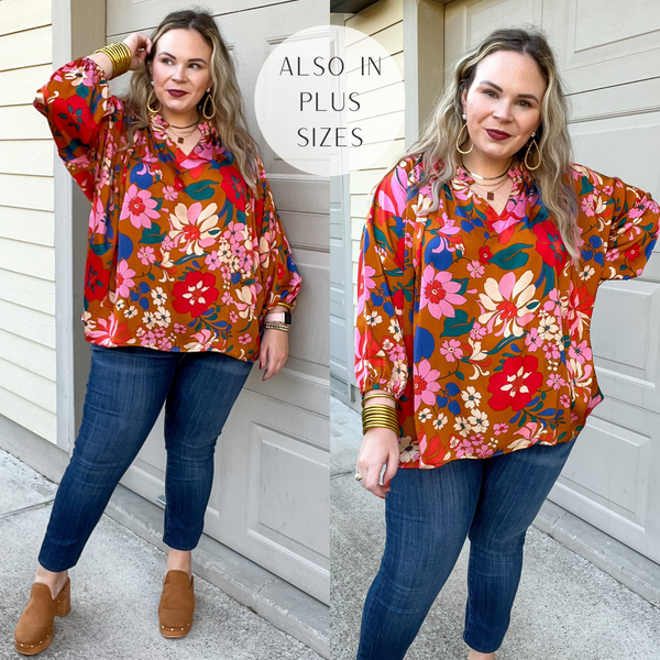Model is wearing a camel brown top with a bright floral print, 3/4 sleeves, and notched neckline. Model has it paired with jeggings, brown clogs, and gold jewelry.